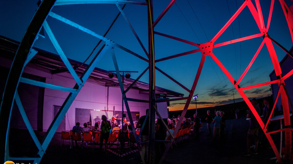 Abendstimmung, Blick auf das Publikum durch beleuchteten Strommast hindurch